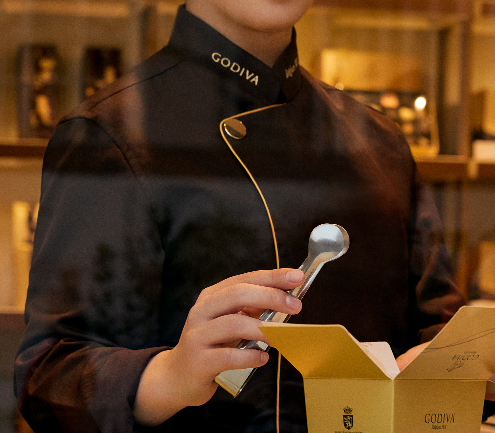 Person in a Godiva uniform holding a spoon over a chocolate box