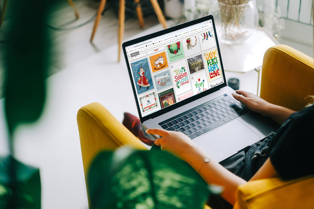 Person browsing holiday cards on a laptop in a cozy chair.