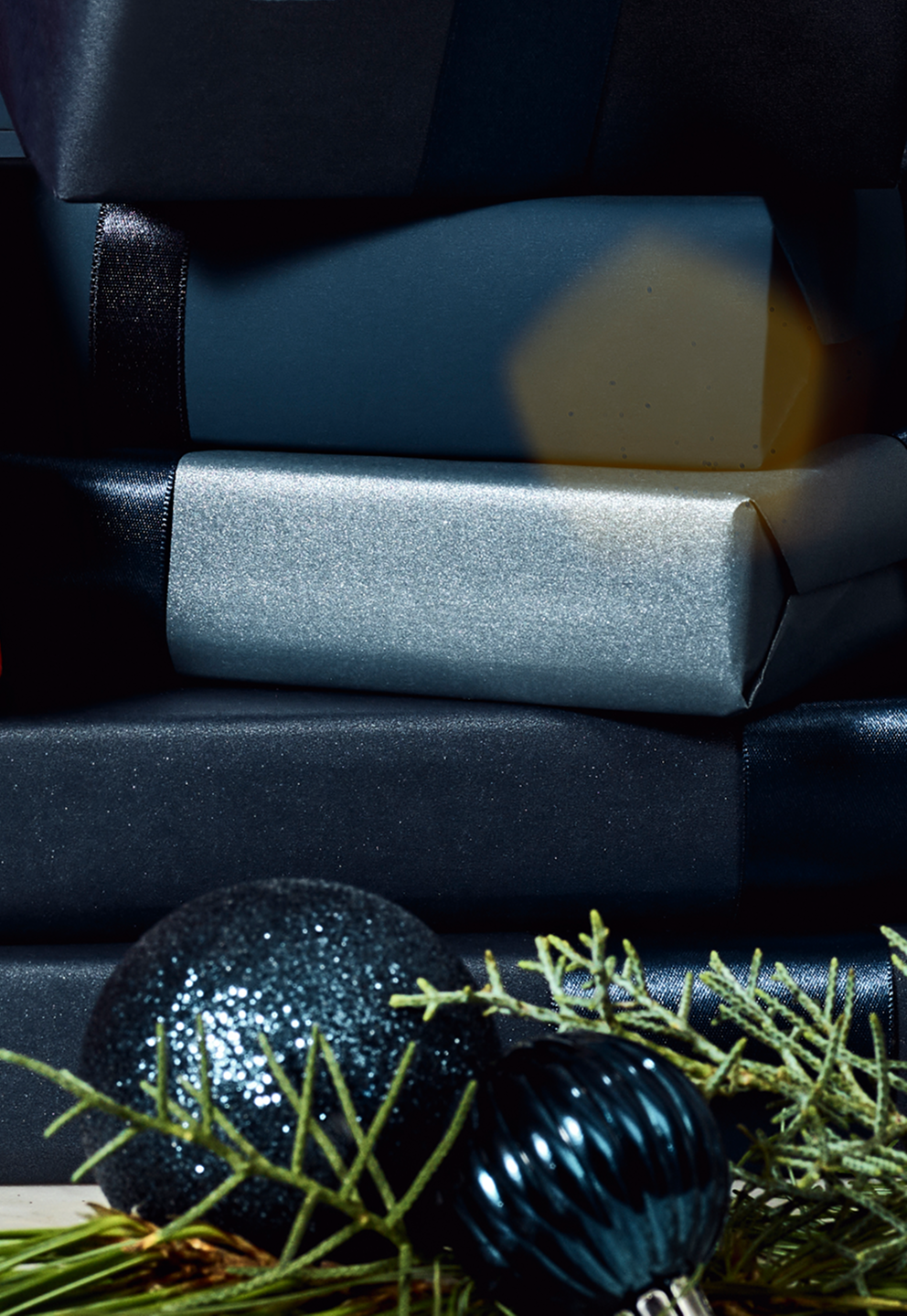 Stack of wrapped presents with a blue and silver box, and decorative blue ornaments on a dark surface.