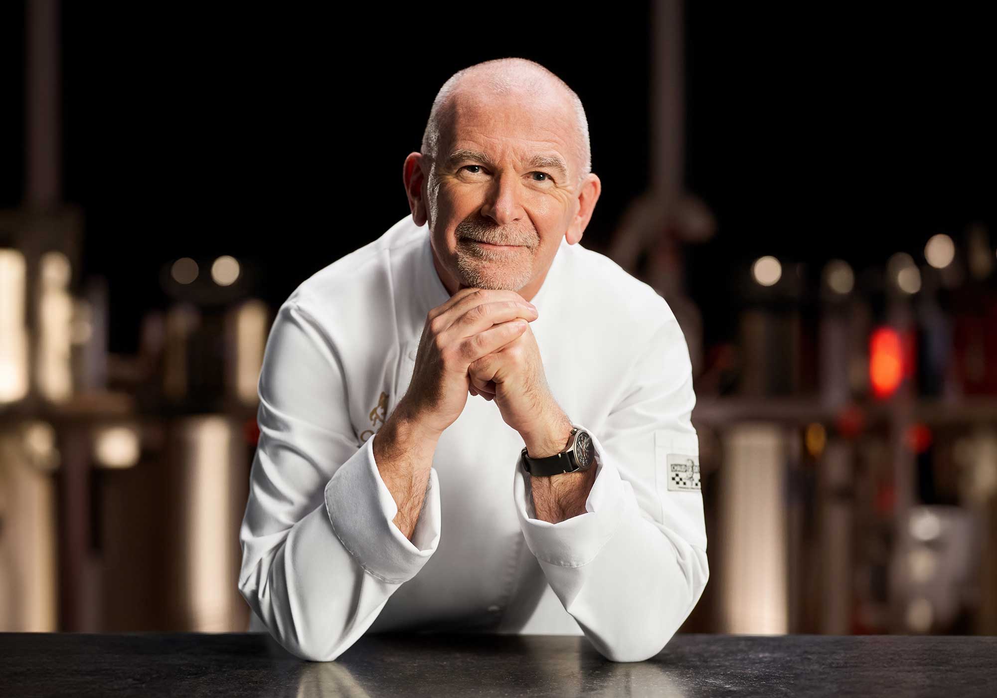 Chef Thierry Muret standing proudly in a kitchen wearing his GODIVA Chef's uniform.